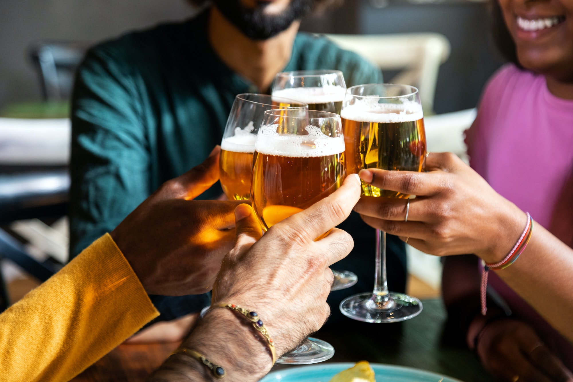 Close up of friends toasting with beer indoors. Friends having fun at bar cheering with beer.